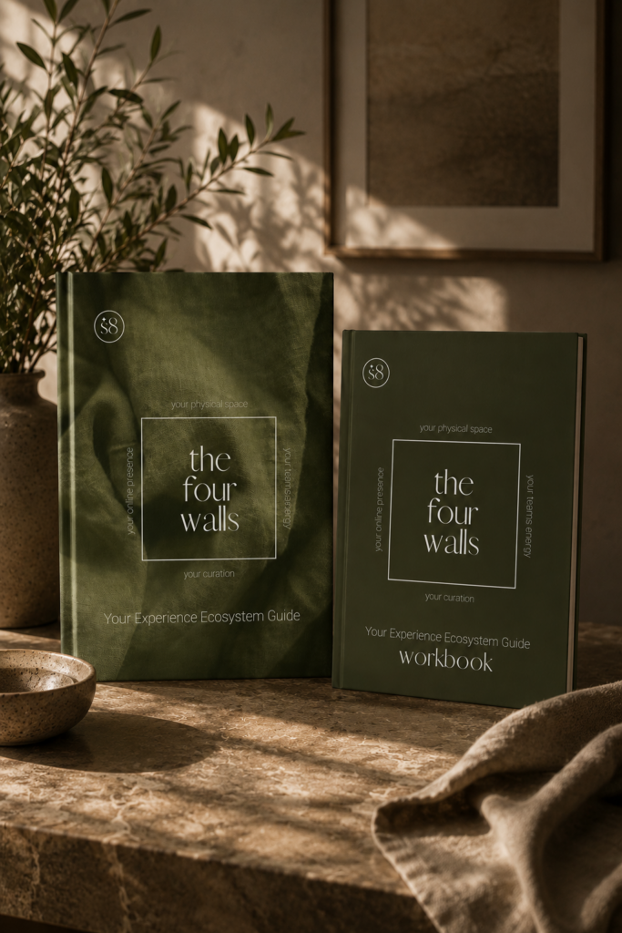 Skinduc8 the four walls handbook and workbook, olive green hardcover books labelled your online presence, your physical space, your team's energy and your curation, styled on a stone table with an olive branch and framed art in warm natural light.