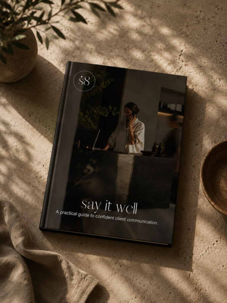 Skinduc8 say it well hardcover book, a practical guide to confident client communication, styled on a stone surface with dappled natural light, a linen throw and a ceramic bowl.
